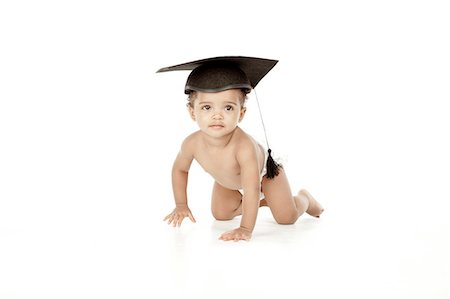 An infant crawling in front of a white background, wearing a graduation cap. Foto de stock - Royalty Free Premium, Número: 6110-06702759