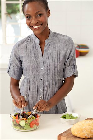 simsearch:6110-06702748,k - Young African woman making food and smiling at camera Foto de stock - Royalty Free Premium, Número: 6110-06702771