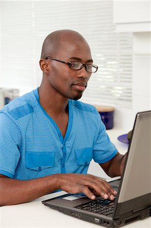 simsearch:6110-06702748,k - Young African man working on a laptop in the kitchen, smiling Foto de stock - Royalty Free Premium, Número: 6110-06702779