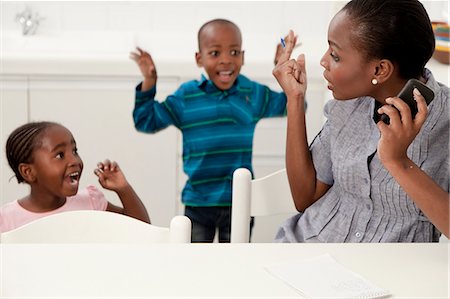 simsearch:6110-06702683,k - Young African mother trying to talk on her cellphone while her children play in the background Stock Photo - Premium Royalty-Free, Code: 6110-06702785