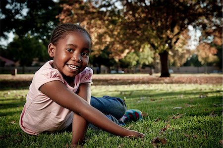 simsearch:6110-06702748,k - Young African girl sits in a park, smiling at camera Foto de stock - Royalty Free Premium, Número: 6110-06702798