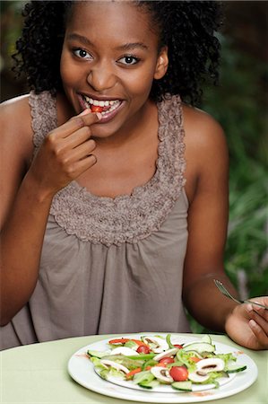 simsearch:6110-06702795,k - Young black woman sitting outdoors, eating a salad Foto de stock - Royalty Free Premium, Número: 6110-06702717