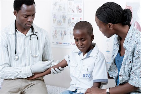 Doctor giving African child an injection in a doctor's room, with a young African woman Fotografie stock - Premium Royalty-Free, Codice: 6110-06702732