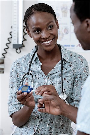 simsearch:6110-06702748,k - Female African doctor checks young African man's blood sugar level Foto de stock - Royalty Free Premium, Número: 6110-06702736