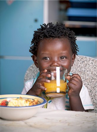simsearch:6110-06702795,k - Young black child drinking orange juice in the kitchen, smiling Foto de stock - Royalty Free Premium, Número: 6110-08968606