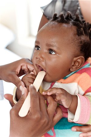 Closeup of a baby African girl with a tongue depressor in her mouth Photographie de stock - Premium Libres de Droits, Code: 6110-08968766
