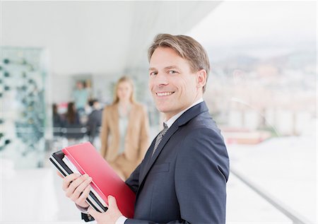 Portrait of smiling businessman holding paperwork in corridor Stock Photo - Premium Royalty-Free, Code: 6113-06497941