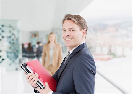 profiles portrait - Portrait of smiling businessman holding paperwork in corridor Photographie de stock - Premium Libres de Droits, Code: 6113-06497941