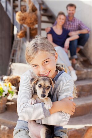 family with one child - Portrait of smiling girl holding puppy with parents in background Stock Photo - Premium Royalty-Free, Code: 6113-06498060
