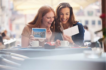 Laughing friends looking at postcards at sidewalk cafe Stock Photo - Premium Royalty-Free, Code: 6113-06498082