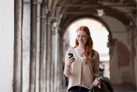 Smiling woman checking cell phone in corridor Stock Photo - Premium Royalty-Free, Code: 6113-06498158