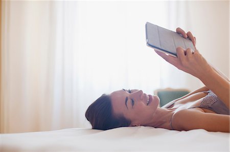 ebook - Smiling woman laying on bed and using digital tablet Stock Photo - Premium Royalty-Free, Code: 6113-06498163