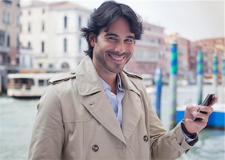 Portrait of smiling man holding cell phone at waterfront in Venice Stock Photo - Premium Royalty-Free, Code: 6113-06498105