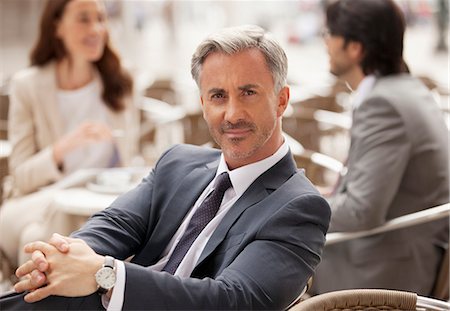 Portrait of smiling businessman at sidewalk cafe with co-workers in background Stock Photo - Premium Royalty-Free, Code: 6113-06498204
