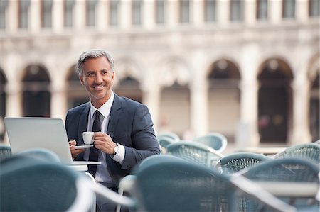 simsearch:6113-06498244,k - Smiling businessman drinking espresso and using laptop at sidewalk cafe Foto de stock - Sin royalties Premium, Código: 6113-06498222