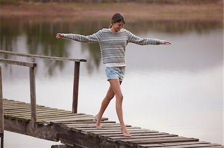 Woman walking on dock over lake with arms outstretched Stock Photo - Premium Royalty-Free, Code: 6113-06498468