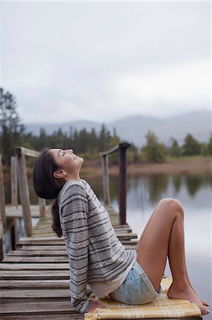 Smiling woman sitting on dock at lakeside with head back Stock Photo - Premium Royalty-Free, Code: 6113-06498479