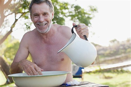 Portrait of smiling man with pitcher washing face in basin at lakeside Stock Photo - Premium Royalty-Free, Code: 6113-06498581