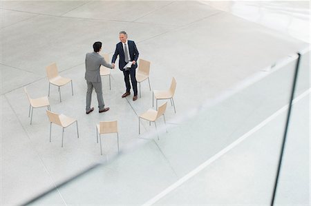 simsearch:6113-06498770,k - Circle of chairs around businessmen shaking hands Foto de stock - Royalty Free Premium, Número: 6113-06498745