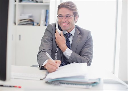 single person working on computer at desk - Smiling businessman talking on telephone and writing Stock Photo - Premium Royalty-Free, Code: 6113-06498904