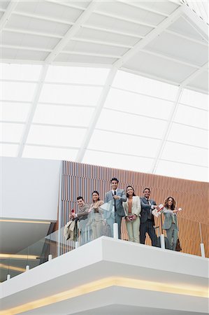 simsearch:6113-07243135,k - Portrait of smiling business people at glass railing of balcony in modern office Foto de stock - Sin royalties Premium, Código: 6113-06498916