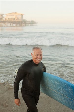 Older surfer carrying board on beach Stock Photo - Premium Royalty-Free, Code: 6113-06499061
