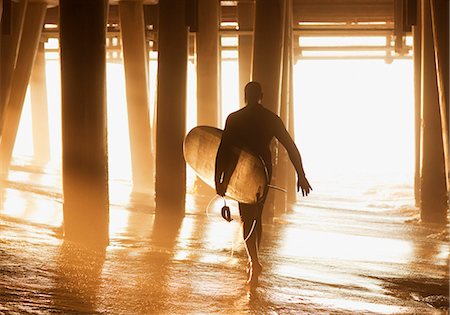 post (structural support) - Older surfer carrying board under pier Stock Photo - Premium Royalty-Free, Code: 6113-06499081