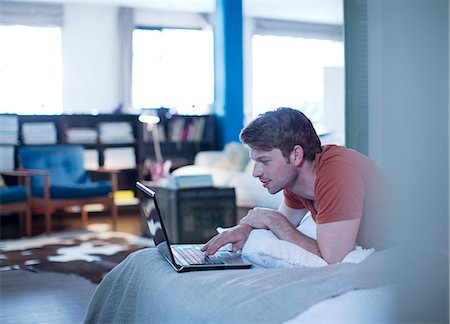 Man using laptop on bed Stock Photo - Premium Royalty-Free, Code: 6113-06625565