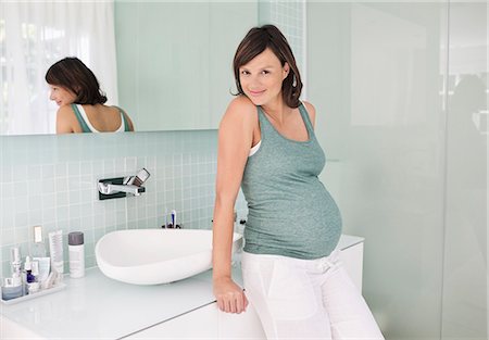 pregnant woman looking at camera - Pregnant woman leaning on bathroom sink Stock Photo - Premium Royalty-Free, Code: 6113-06753599