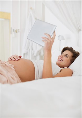 pregnant woman holding her stomach - Pregnant woman using tablet computer on bed Foto de stock - Sin royalties Premium, Código: 6113-06753654