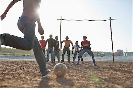 Boys playing soccer together in dirt field Foto de stock - Sin royalties Premium, Código: 6113-06753761