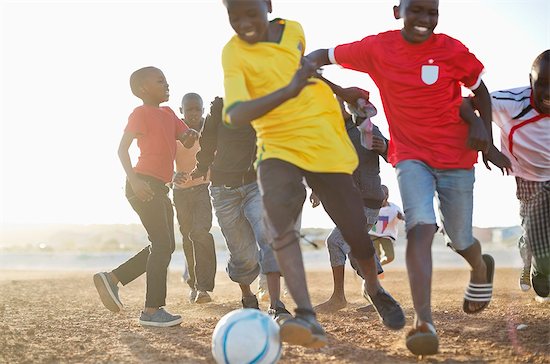 Boys playing soccer together in dirt field Foto de stock - Sin royalties Premium, Código de la imagen: 6113-06753811