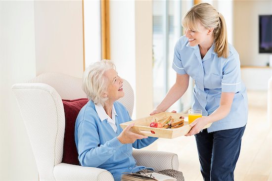 Caregiver giving older woman tray of food Stock Photo - Premium Royalty-Free, Image code: 6113-06720661