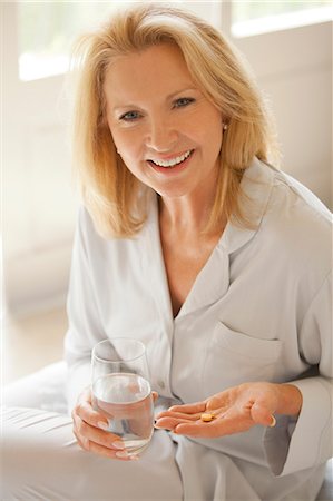 Portrait of smiling woman holding pill and glass of water Stock Photo - Premium Royalty-Free, Code: 6113-06898862