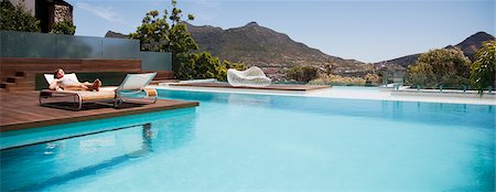 Woman sunbathing on lounge chair next to luxury swimming pool with mountain view Stock Photo - Premium Royalty-Free, Code: 6113-06898822