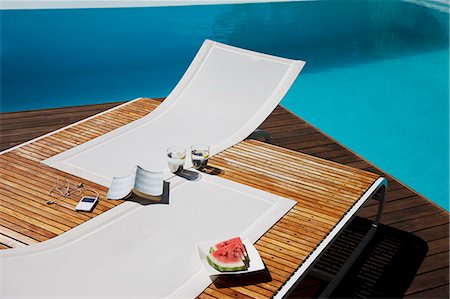 Book, mp3 player, water and watermelon on lounge chairs at poolside Foto de stock - Sin royalties Premium, Código: 6113-06898833