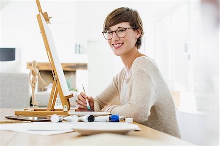 female artist painting at easel - Portrait of smiling woman painting at easel on table Stock Photo - Premium Royalty-Free, Code: 6113-06898956