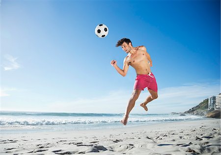 simsearch:6113-06626093,k - Man in swim trunks heading soccer ball on beach Fotografie stock - Premium Royalty-Free, Codice: 6113-06899176