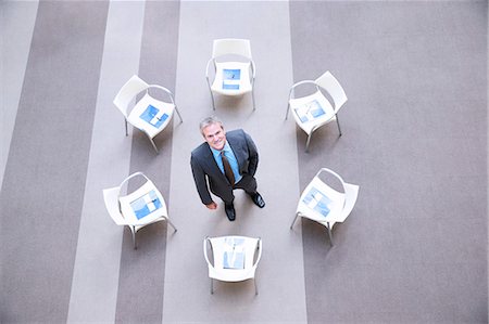 High angle portrait of smiling businessman at center of chairs in circle Foto de stock - Sin royalties Premium, Código: 6113-06899118