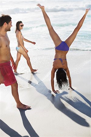 Friends watching woman in bikini doing handstand on beach Foto de stock - Sin royalties Premium, Código: 6113-06899255