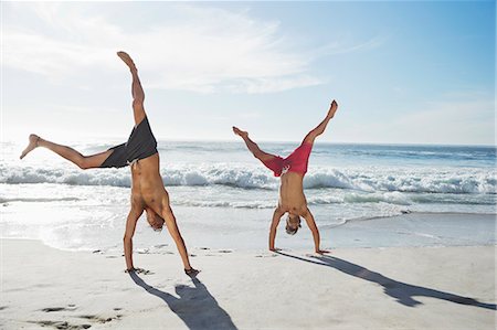 sun light - Men in swim trunks doing handstands on beach Stock Photo - Premium Royalty-Free, Code: 6113-06899262