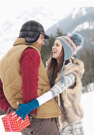 Woman reaching for Christmas gift behind man's back in snowy field Stock Photo - Premium Royalty-Free, Code: 6113-06899424