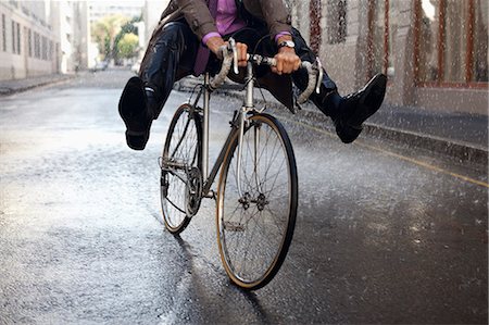 Businessman riding bicycle with feet up in rain Stock Photo - Premium Royalty-Free, Code: 6113-06899551