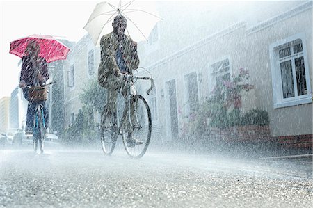 Couple with umbrellas riding bicycles in rain Stock Photo - Premium Royalty-Free, Code: 6113-06899569