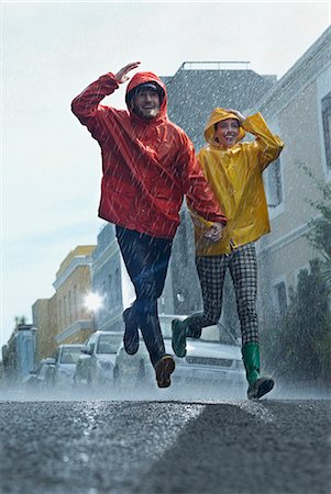 Happy couple in raincoats running down street in rain Stock Photo - Premium Royalty-Free, Code: 6113-06899572