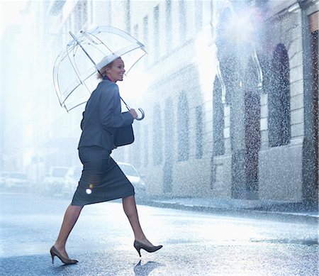 Happy businesswoman with umbrella walking across rainy street Photographie de stock - Premium Libres de Droits, Code: 6113-06899596