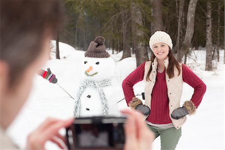 Man photographing smiling woman with hands on hips next to snowman in woods Stock Photo - Premium Royalty-Free, Code: 6113-06899505