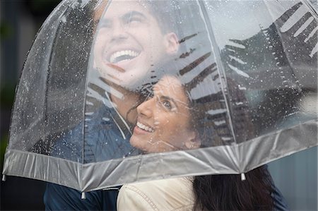 sharing umbrella - Happy couple under umbrella looking up at rain Stock Photo - Premium Royalty-Free, Code: 6113-06899648