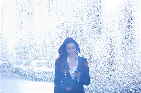 Happy businesswoman text messaging with cell phone in rain Stock Photo - Premium Royalty-Free, Code: 6113-06899662
