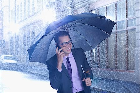 Happy businessman talking on cell phone under umbrella in rainy street Photographie de stock - Premium Libres de Droits, Code: 6113-06899677